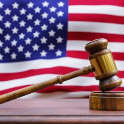 A wooden gavel resting on a judges bench with the American flag in the background.