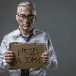 Desperate unemployed messy businessman holding a torn cardboard sign and looking at camera, he needs a job