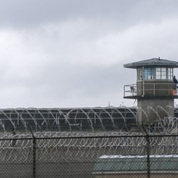 An armed guard surveys the grounds from the railing of a prison watchtower