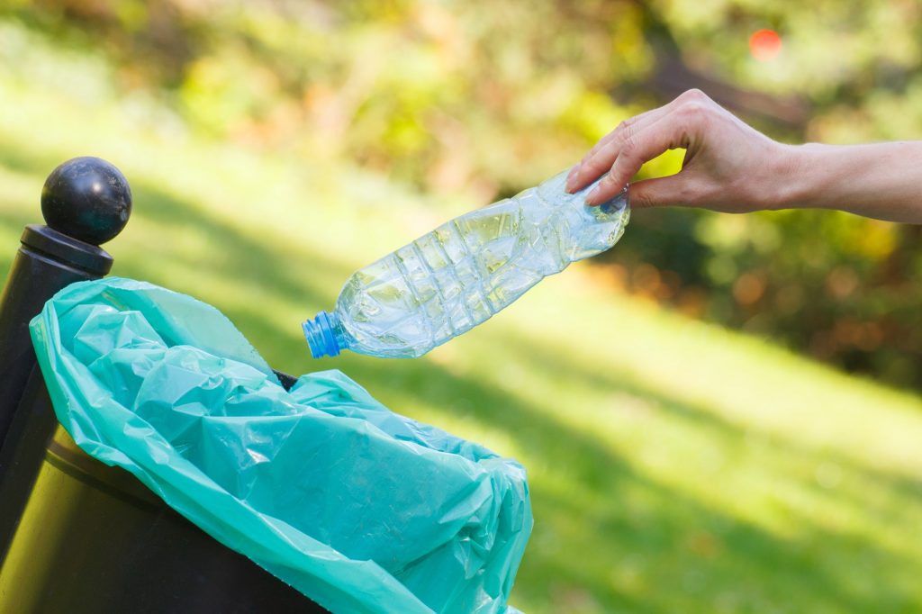Hand of woman throwing bottle into recycling bin, littering of environmental