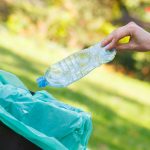 Hand of woman throwing bottle into recycling bin, littering of environmental