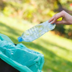 Hand throwing plastic bottle into old trash can, concept of environmental protection, littering of environmental