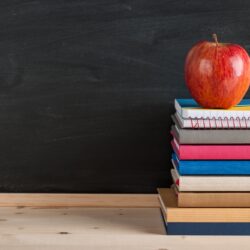 Red apple top a stack of books and notebooks on blackboard background