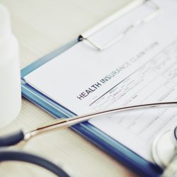 Close-up image of health insurance document, stethoscope and pills