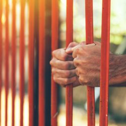 Male hands behind prison yard bars, incarcerated captivated person in jail