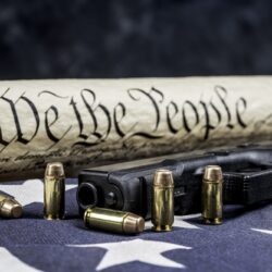 A handgun with bullets symbolizing gun rights while framed against the United States constitution.