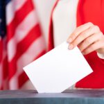 American voter putting ballot into voting box.