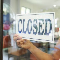 Close-up of saleswoman hanging the Closed sign on glass door and closed the store