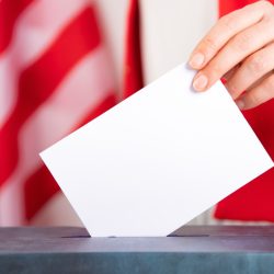 American voter putting ballot into voting box.