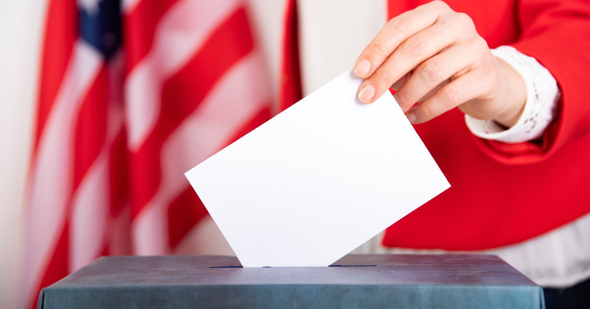 American voter putting ballot into voting box.